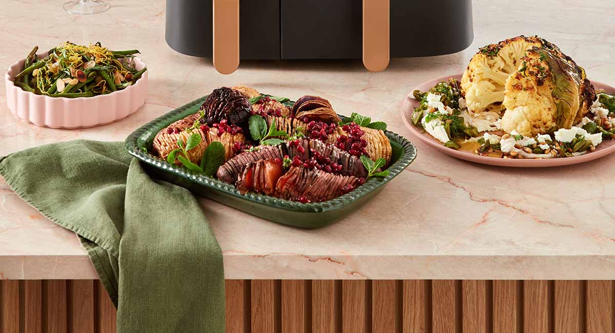 A selection of side dishes including, from left to right, air-fried green beans, air-fried hasselback root vegetables and a whole air-fried cauliflower.