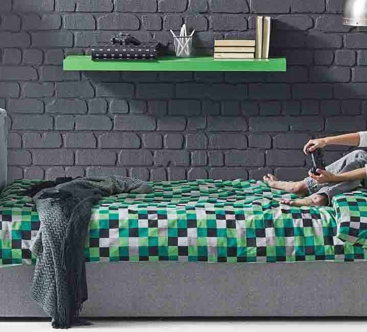 A teen using his bed with hydraulic TV lift to play video games.