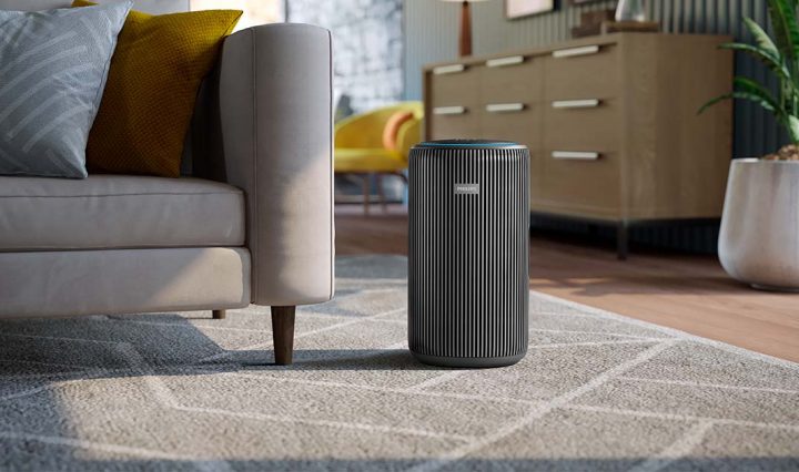An air purifier on a rug in a room next to a sofa.