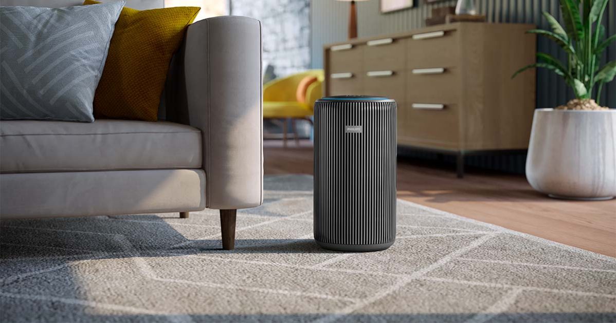 An air purifier on a rug in a room next to a sofa.