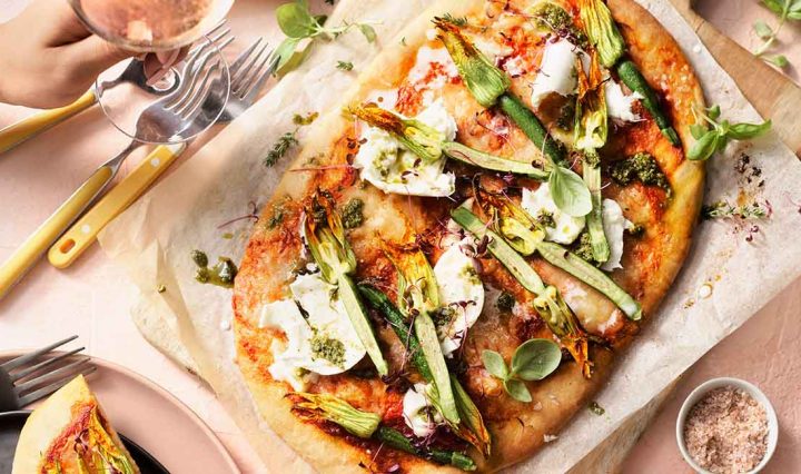 A pizza on a serving board. The pizza is topped with zucchini flowers, buffalo mozzarella and basil pesto.