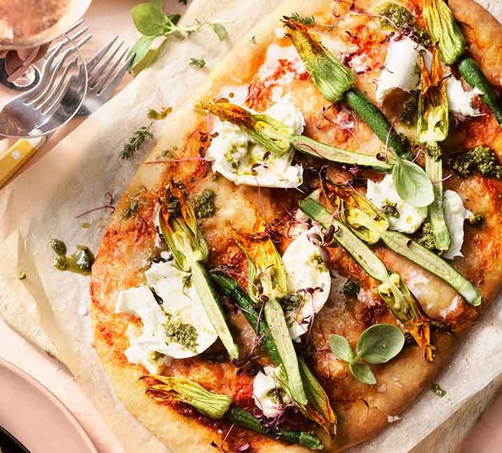 A pizza on a serving board. The pizza is topped with zucchini flowers, buffalo mozzarella and basil pesto.