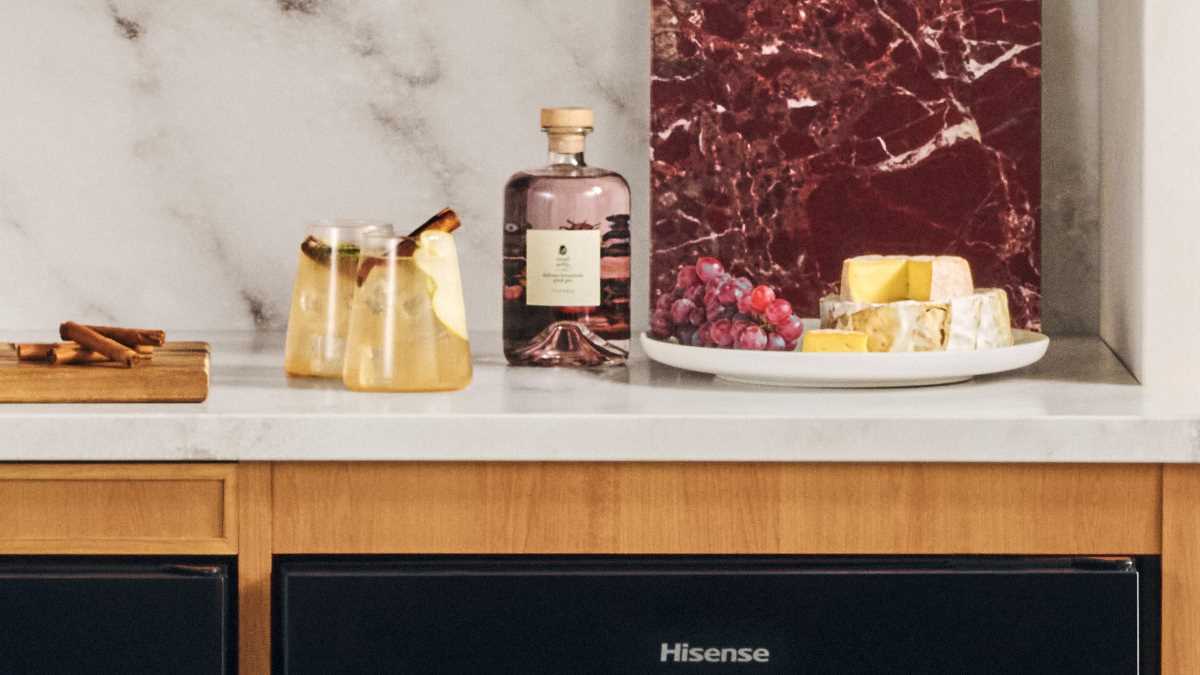 White kitchen countertop showing two Spiced Pear Mules in stemless glasses. A serving platter and bottle of liquer is to the right, with a soft cheese and berries on the serving platter as a suggestion.