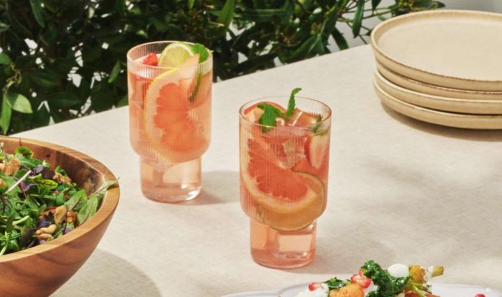 Two glasses are set on top of a white table, each filled with the Rosé and White Nectarine Sangria, garnished with orange slices and mint.