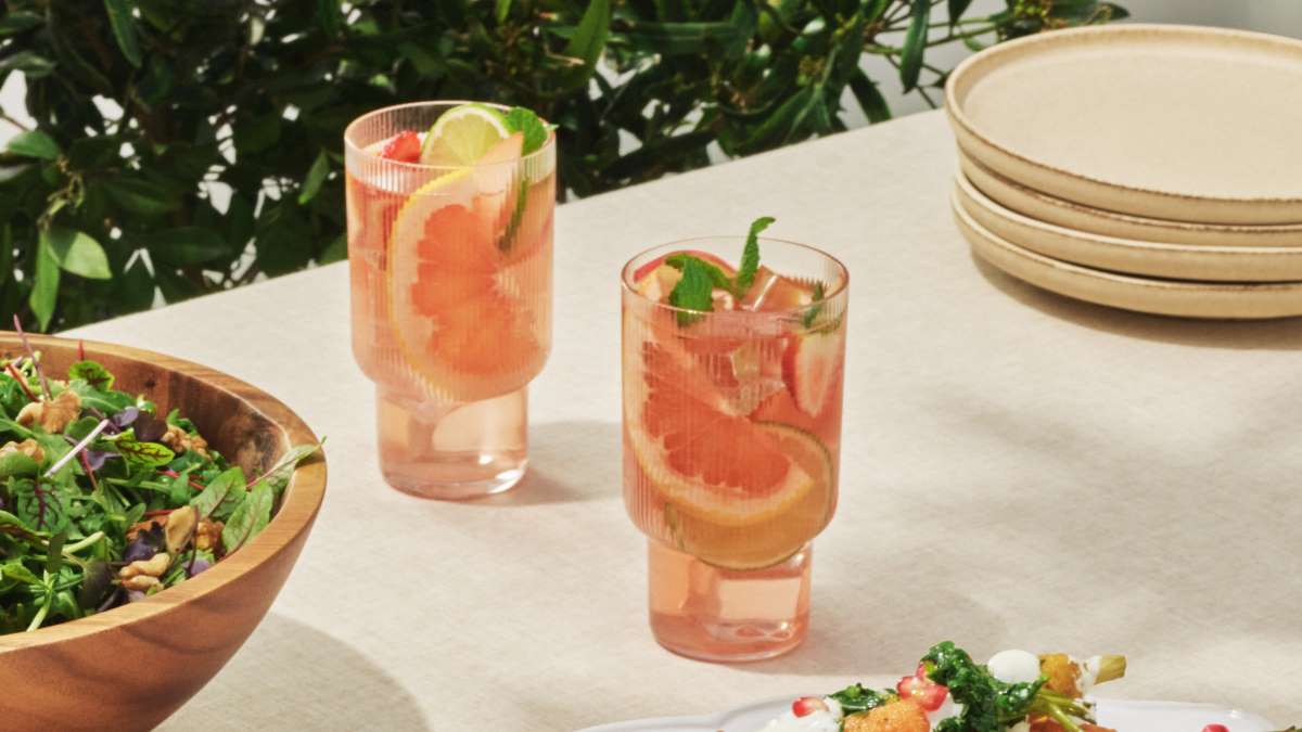 Two glasses are set on top of a white table, each filled with the Rosé and White Nectarine Sangria, garnished with orange slices and mint.