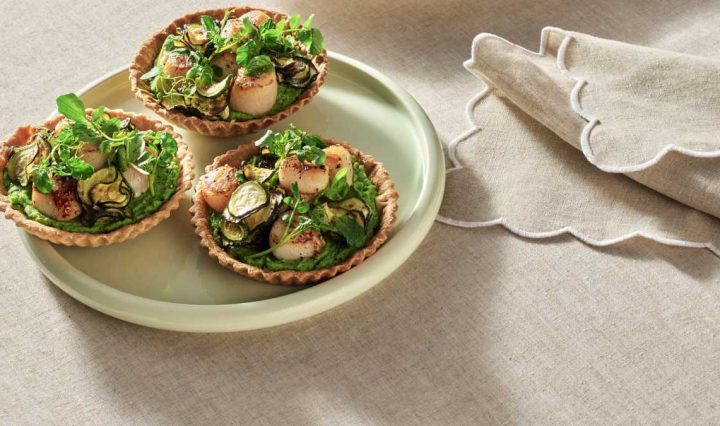 A light green plate showing three of the finished Zucchini and Pea Tarts with Seared Scallops ready to serve.