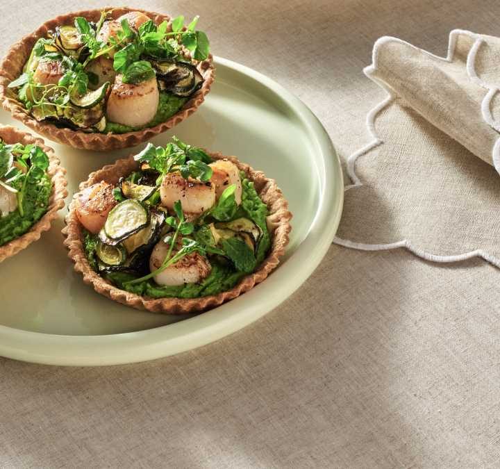 A light green plate showing three of the finished Zucchini and Pea Tarts with Seared Scallops ready to serve.