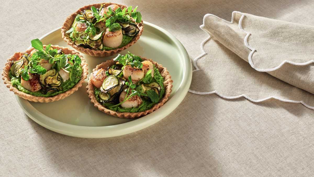 A light green plate showing three of the finished Zucchini and Pea Tarts with Seared Scallops ready to serve.